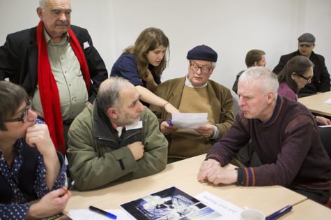 A group of six people sitting round a table, looking a resources of On The Record.