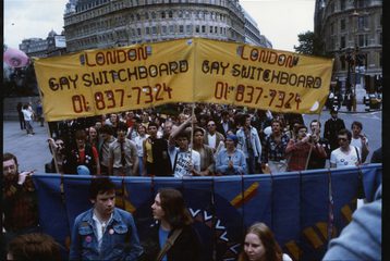 A photo from Pride, where crowds are in central London with the sign "London gay switchboard".