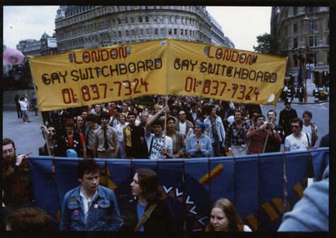 A photo from Pride, where crowds are in central London with the sign "London gay switchboard".