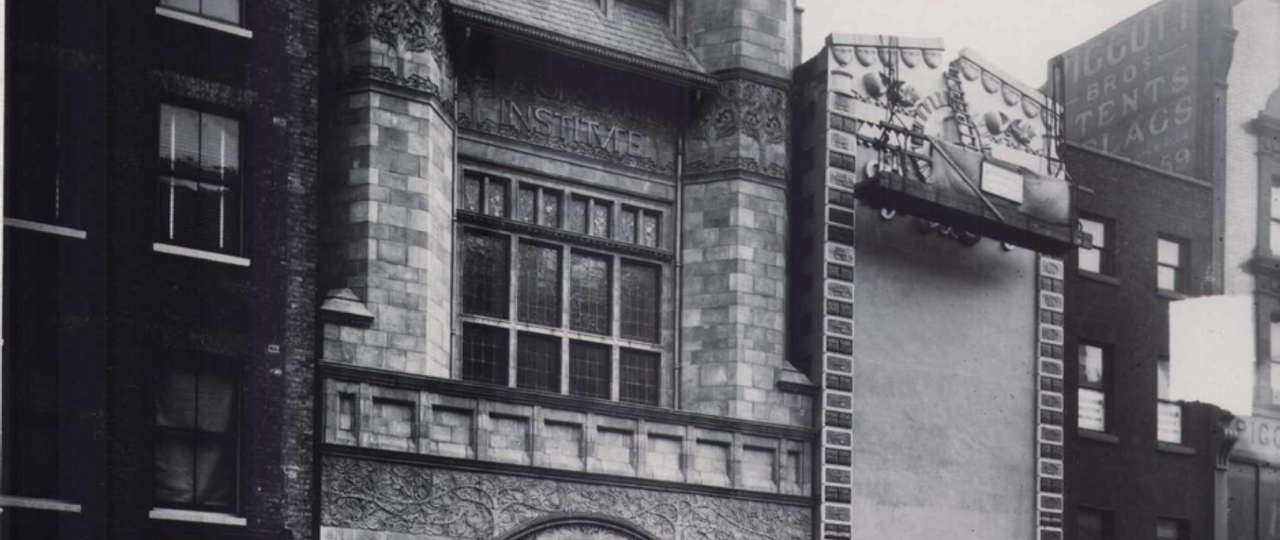 A photo of the exterior of Bishopsgate Institute in 1895. It has two turrets, and a circular archway to enter.