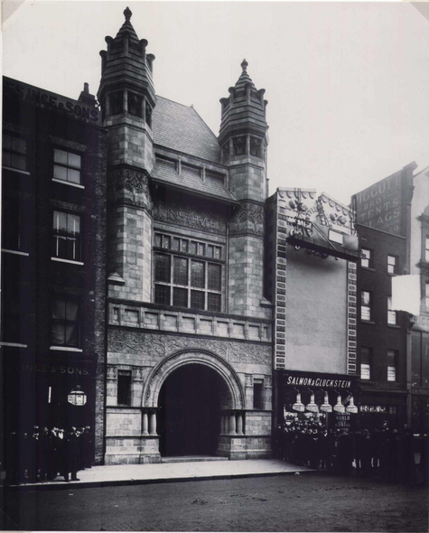 A photo of the exterior of Bishopsgate Institute in 1895. It has two turrets, and a circular archway to enter.