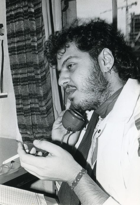 A black and white photograph of a man on the phone at the Switchboard office. The phone is in his right hand a cigarette in his left hand.