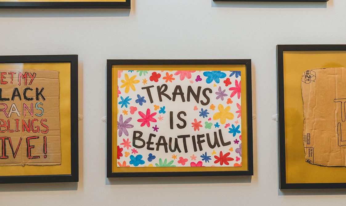 A photograph of a framed placard from a the Black Trans Lives Matter march. The placard says 'Trans is Beautiful', and the words are surrounded by stars and flowers in multicolours.