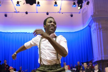 Image from our collection of a man Swing dancing with a brace on and a group of people watching on from behind.