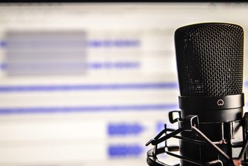 A podcast microphone is in focus, with the back of the image being audio editing software.