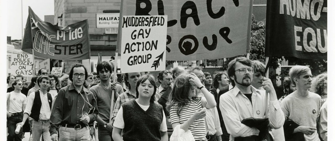 Gay pride Hudderfield 1981. The marchers are holding signs which say: "Gay Black Group", "Muddersfield Gay Action Group".