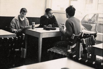 Three people are sitting in a cafe talking. This is a black and white photo from the New Left Archive.
