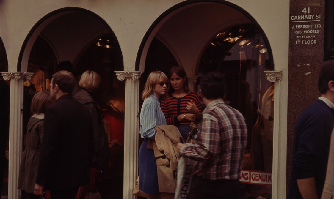 A photo taken outside the "Clothes" shop on Carnaby Street in the 1960s. People are talking to each other outside the shop.