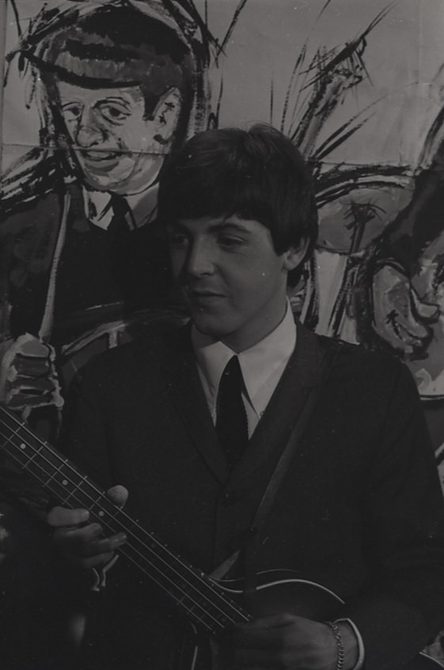 A portrait black and white photo of Paul McCartney playing his guitar.