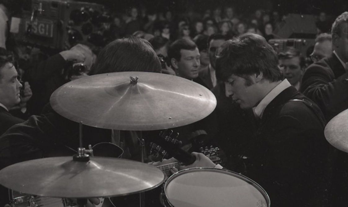 An image taken at a concert for the Beatles. The focus of the image is the drum kit and the crowd in front.