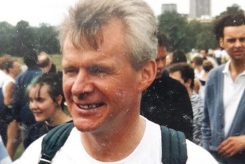 A photograph of Bob Cant at 1988 Pride. He is wearing a top that says "Lesbian Gay", and has a rucksack on. A group of people are standing behind him.