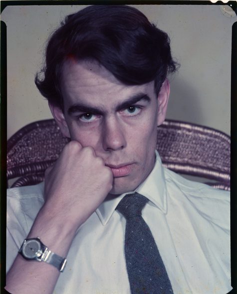 An image of photographer Derek Brook. He is wearing a white shirt and a tie, and has short black hair. He is resting is head on his hand.