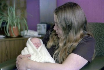A woman is holding a newborn baby wrapped in a shawl.