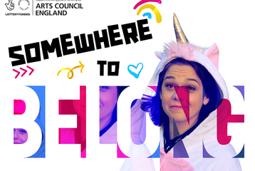 A poster with the words "Somewhere to belong". There is also a young person wearing a unicorn onesie, with a hood.