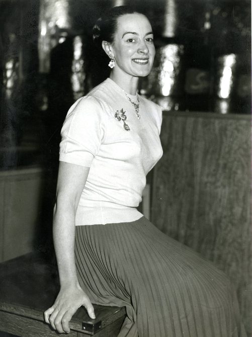 A photo of Peggy Spencer sitting down, she's wearing a black pleated skirt and a white top.