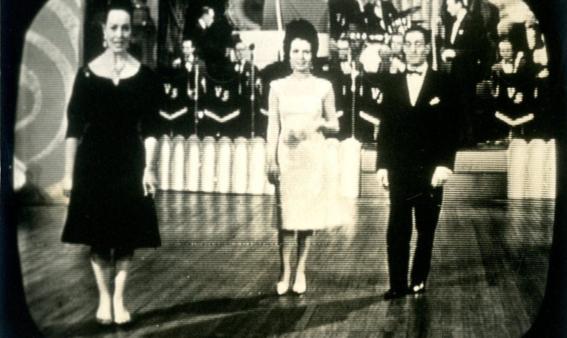 A photo taken of a television screen where two dancers are about to perform. A band is behind them.