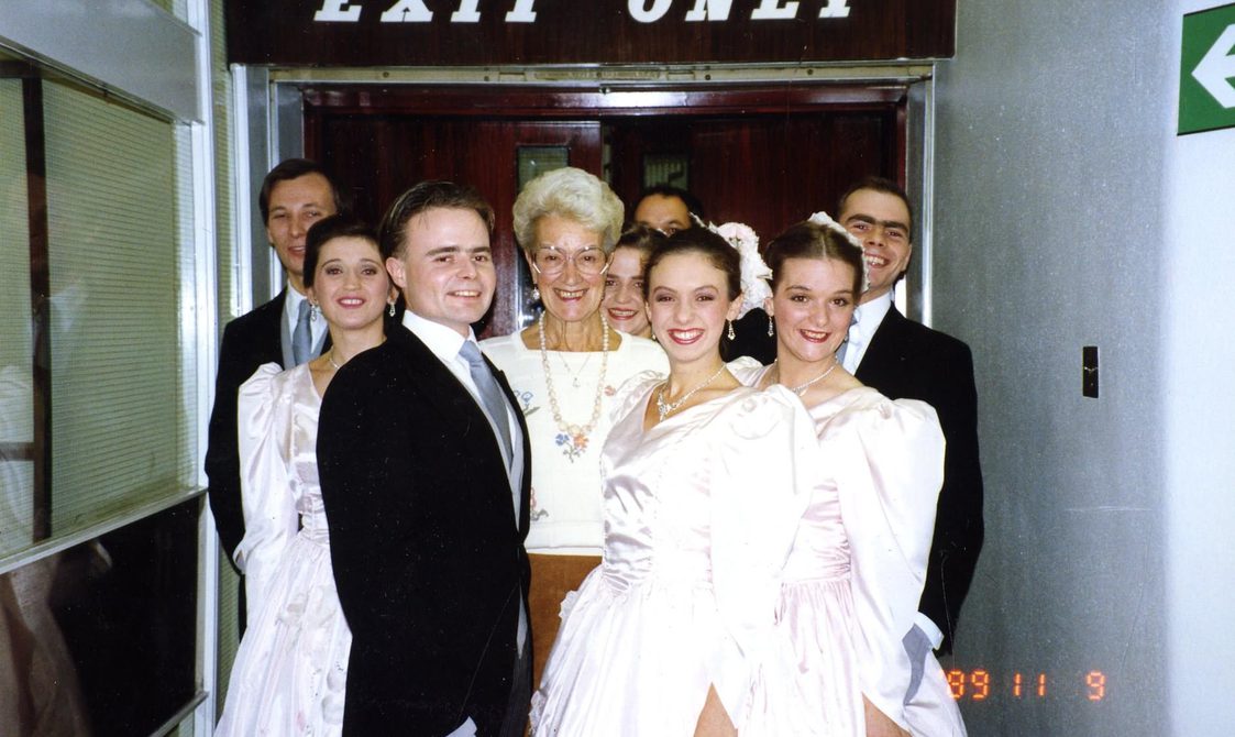 A photo of Peggy Spencer with seven dancers, standing beneath an "Exit Only" sign.