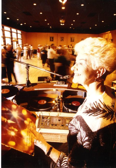 Peggy Spencer standing behind a DJ booth at a dance.