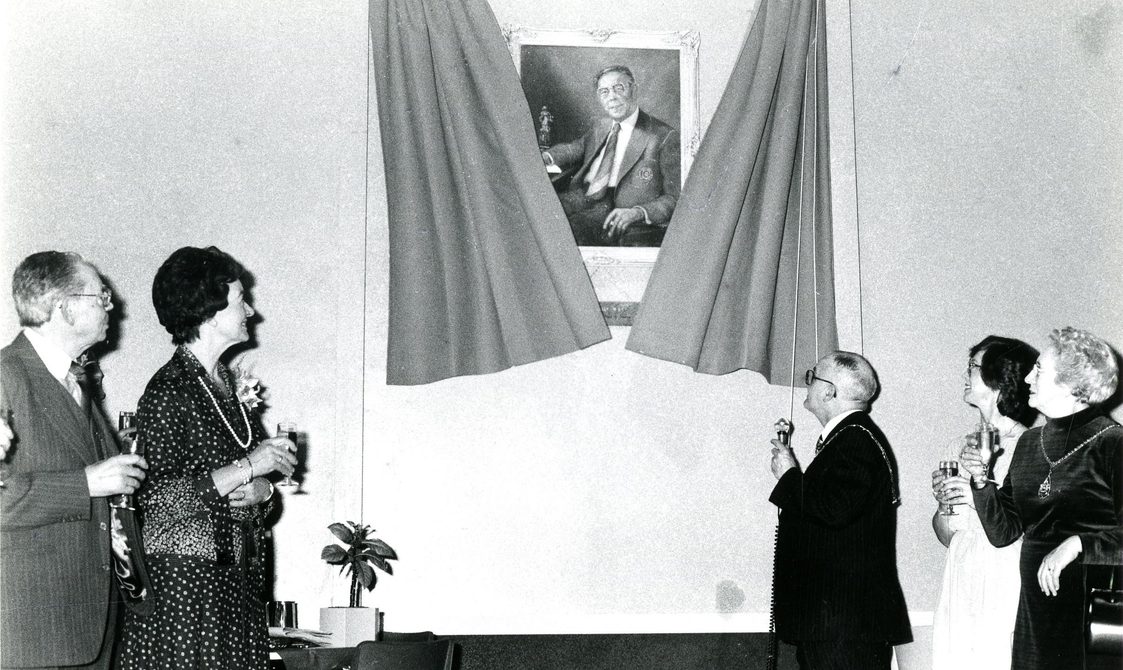 Peggy Spencer and four other people at an unveiling of a portrait image. They are all looking at the photo.
