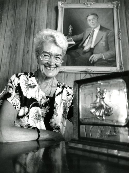 Peggy Spencer with the Formation trophy. She is sitting down the trophy is on a table to her left. She's looking at the camera and the photo is in black and white.