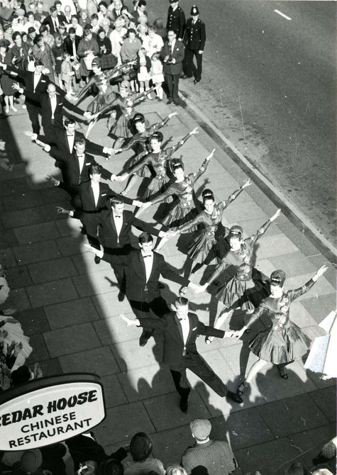 A row of dancers performing on a street. This photo is part of the Peggy Spencer Archive.