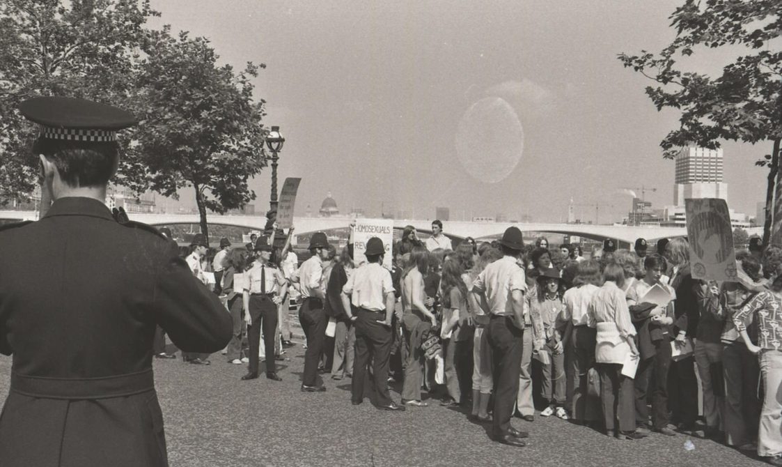 A picture from the second Pride march in 1973. A group of people are marching down from Embankment to Hyde Park. Police officers are around the marchers.
