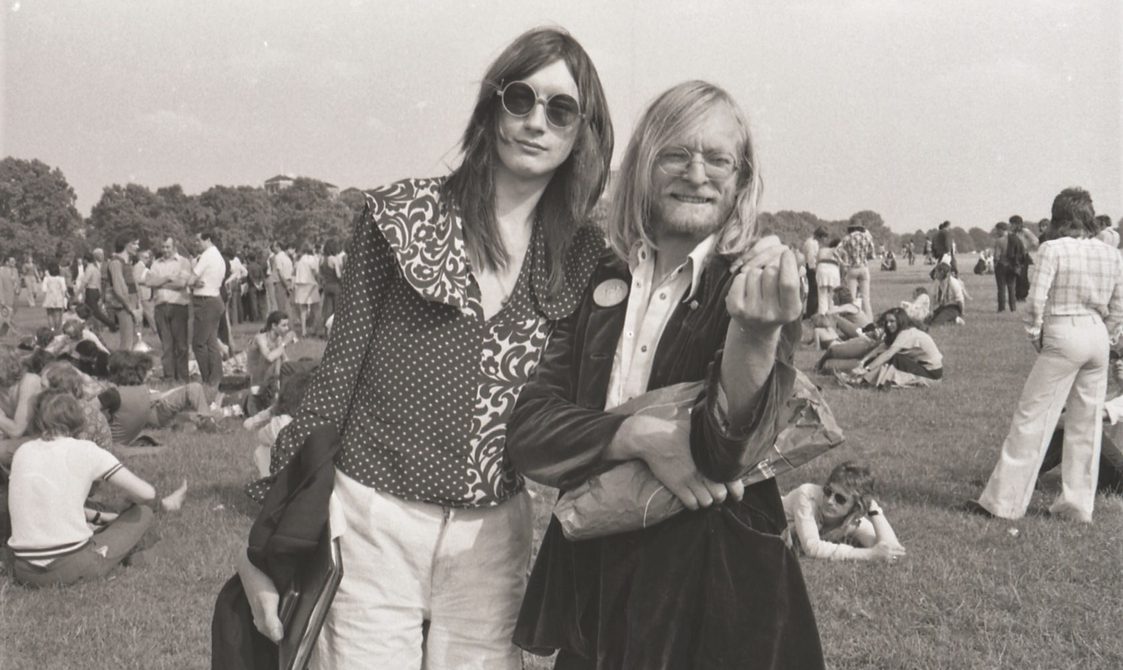 A picture from the second Pride march in 1973. Two people have their arms around each other, while other protestors are sitting in the background.