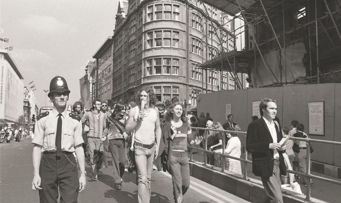 A picture from the second Pride march in 1973. Marchers are walking down the road in Central London, with a police officer next to them.