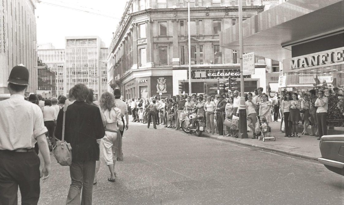 A picture from the second Pride march in 1973. Marchers are walking down the road, with police officers with them.