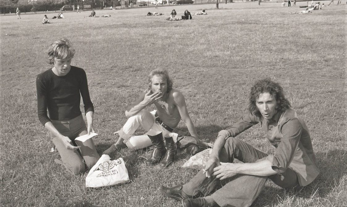 A picture from the second Pride march in 1973. Three people are sitting down on the grass in Hyde Park.