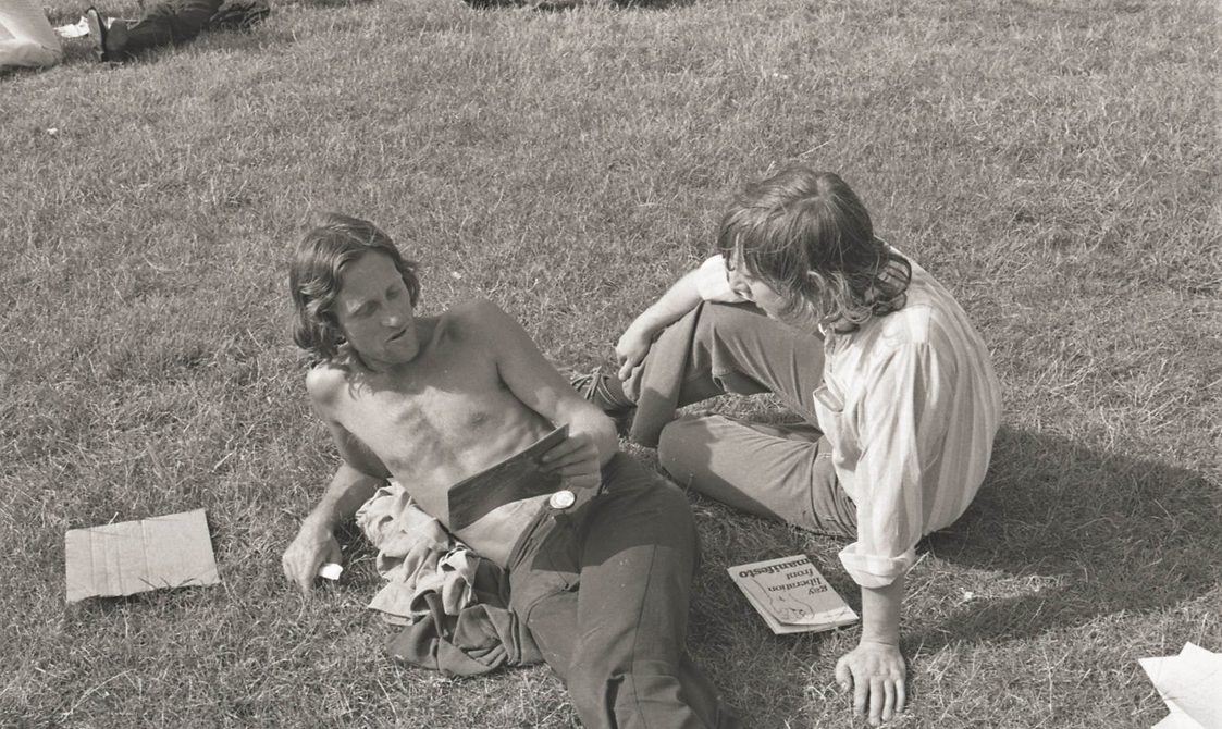 A picture from the second Pride march in 1973. Two people are sitting on the grass in Hyde Park, reading.