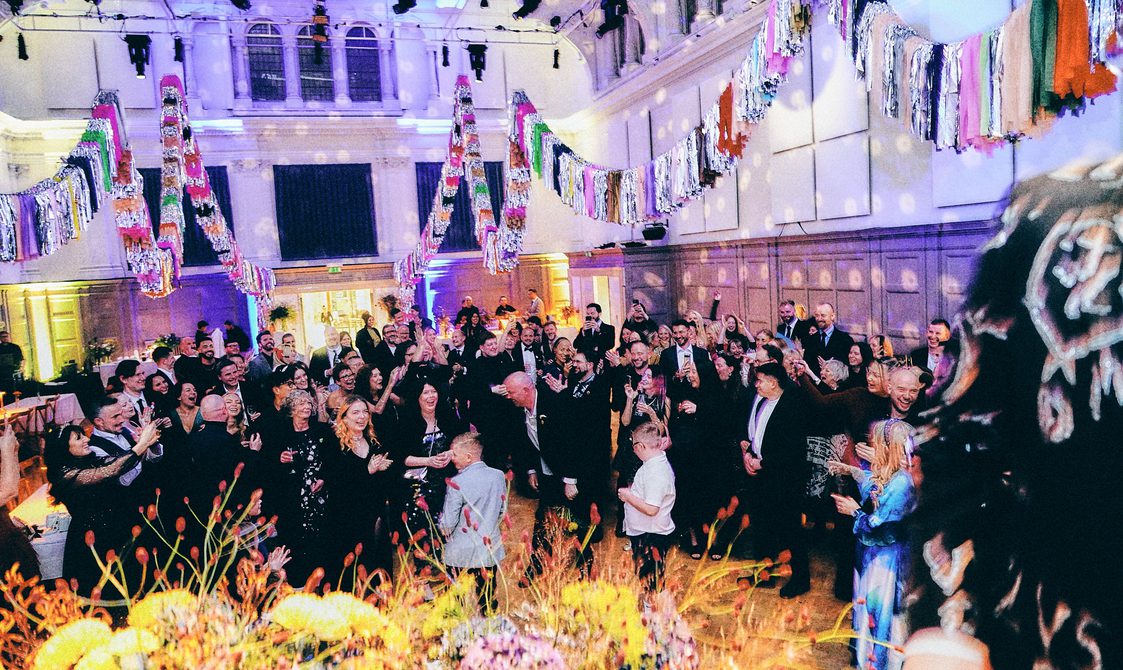 People dancing in a large hall which has been lit up for a disco and colourfully decorated.
