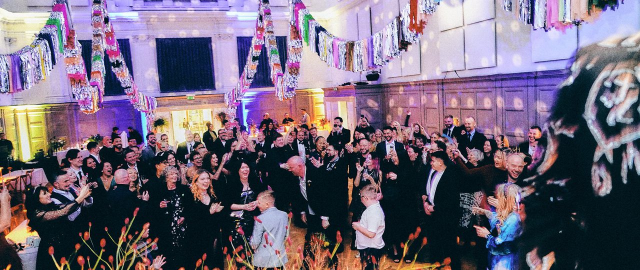 People dancing in a large hall which has been lit up for a disco and colourfully decorated.
