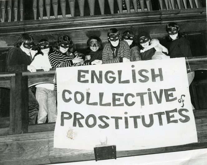 A group of masked sex workers unfurl a banner over the balcony of a church that says "English Collection of prostitutes"