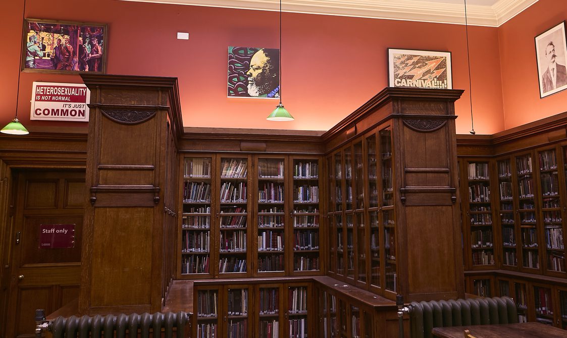 A landscape photo of Bishopsgate Institute Library. The floor is laminate wood flooring, with books in cabinets around the edges of the room.