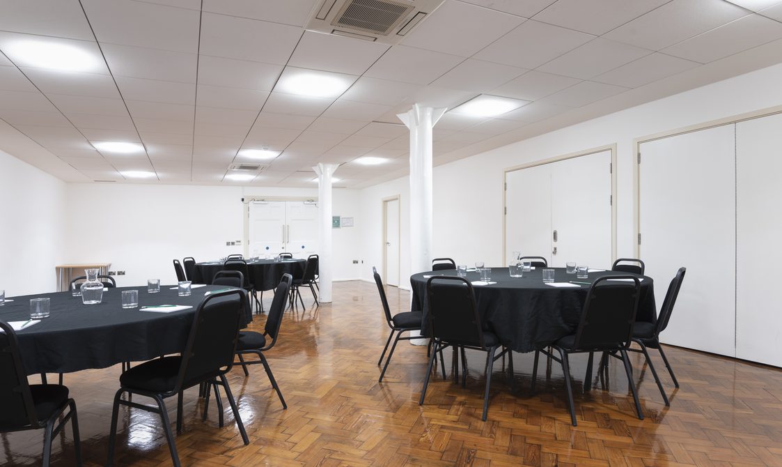 A photograph of the Goss Room at Bishopsgate Institute London. The tables are set out in a cabaret style with chairs around them.