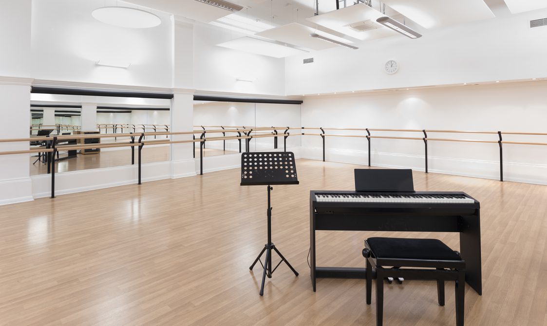 A photograph of Bishopsgate Institute's studio in Central London. There are full length mirrors on the floor and a bar going around the room. There is a keyboard in the room with a stool.