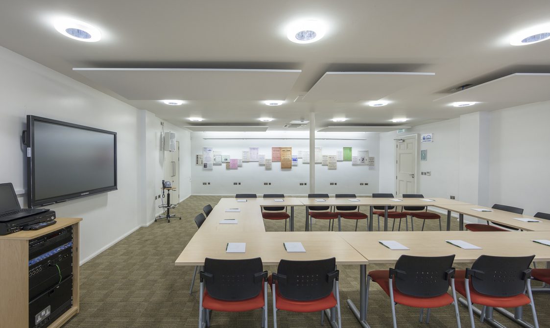 A photograph of the Courtyard Room, with tables set up in a boardroom style. There is a screen at the front for presentations.