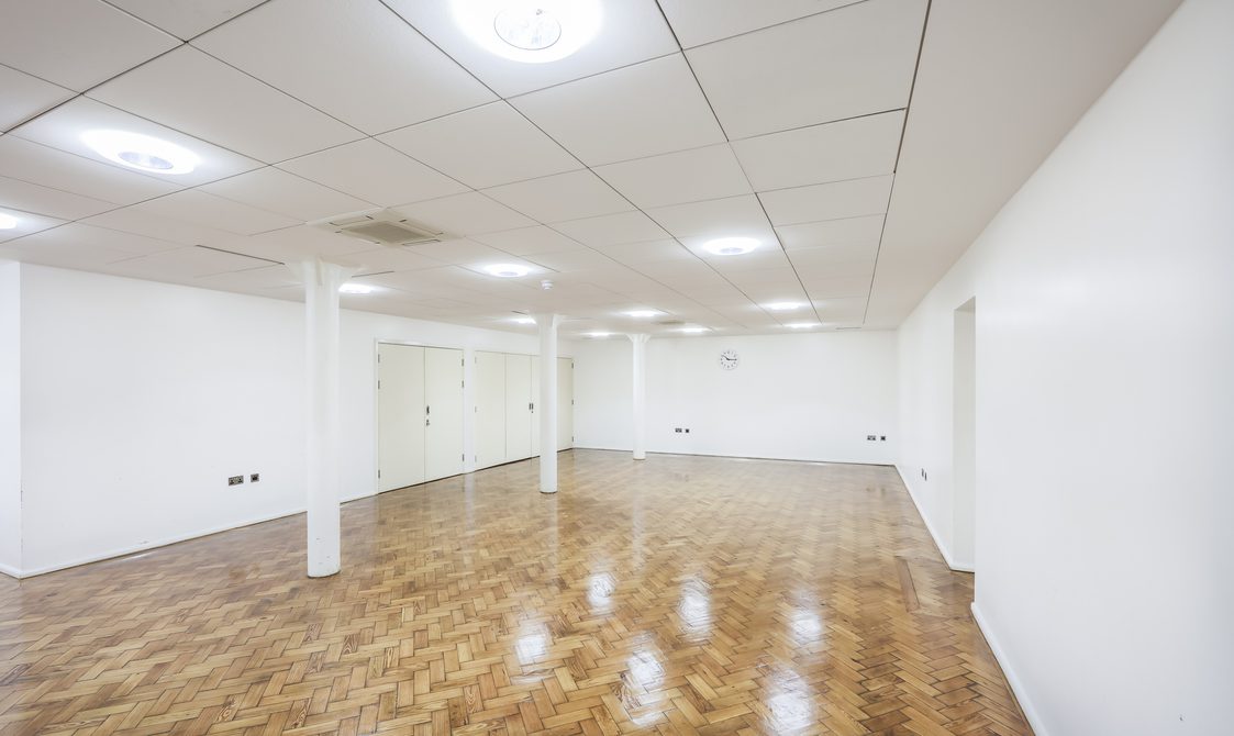 A photograph of the Goss Room. The floor is laminate, with white walls and white beams. There are spotlights in the ceiling.