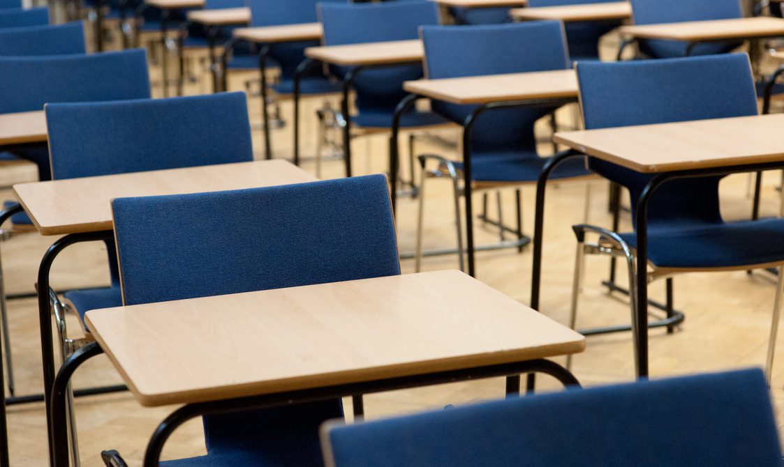 A photograph of exams taking place in the Great Hall. There are rows of single desks with blue chairs behind each desk.