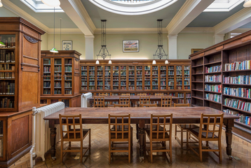 Bishopsgate Institute's Library in central London. There are bookcases on the shelves and a wooden table with chairs in the middle of the room. There is a doom light in the ceiling.