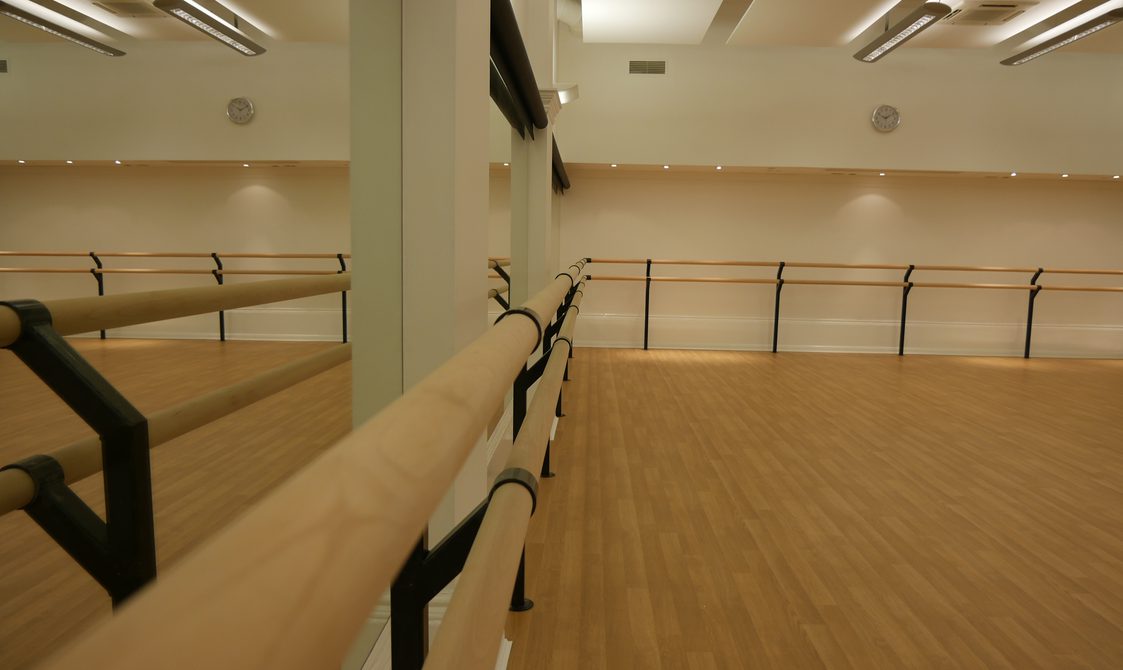 A photograph of the studio at Bishopsgate Institute. The floor is wooden and the walls are painted white with mirrors on some of the walls. There are also dance bars.