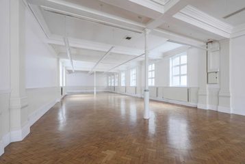 A photograph of Bishopsgate Institute's Upper Hall. The walls are white with white beams in the centre of the room.