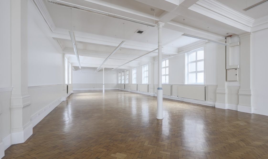 A photograph of the Upper Hall with natural light coming through. The floor is laminate and the walls are white with white beams in the centre of the room.
