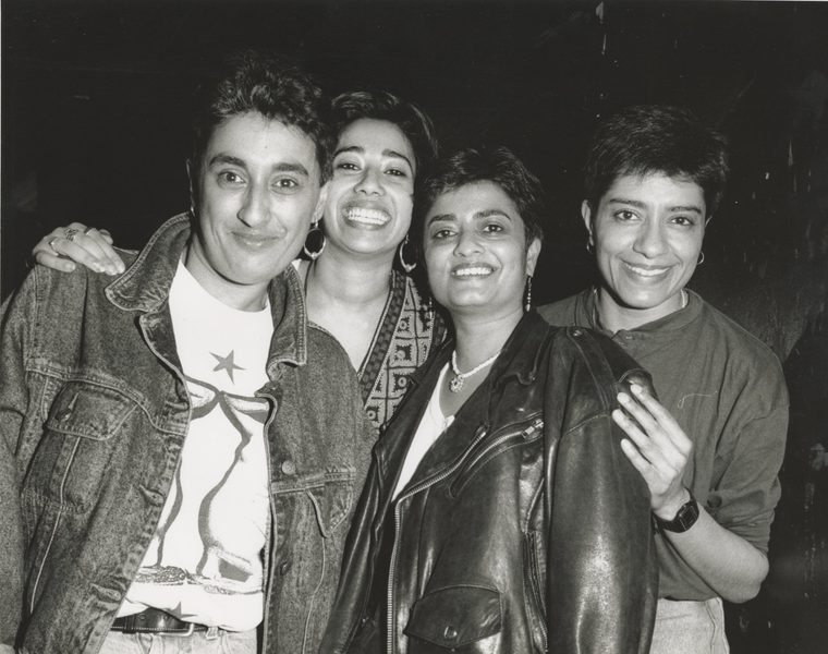 A black and white picture of four South Asian women looking at the camera and smiling