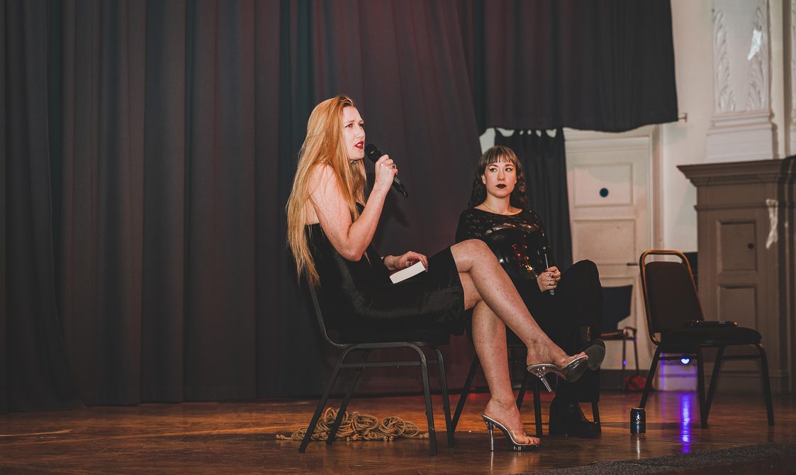 Writers Stacey Clare and Anastasiia Fedorova seated on stage in the Great Hall. Stacey is speaking into the microphone.