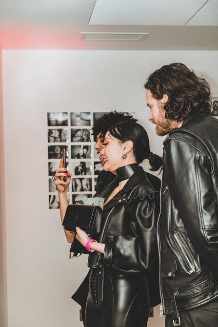 Dominatrix Eva Oh taking a selfie with two people. Behind them is a photography display.