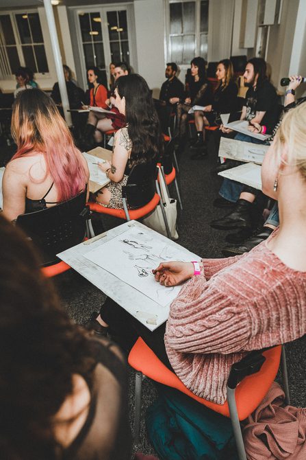 A group of people seated at desks, drawing in charcoal.