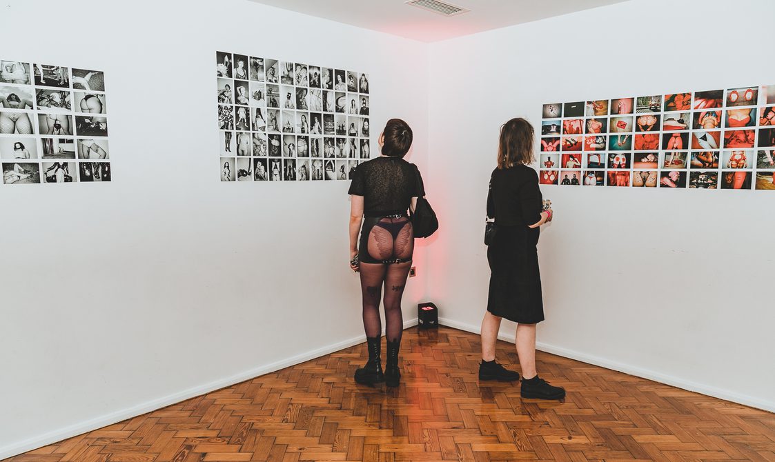 Two people looking at a display o photographs from the Kink and Fetish archives.