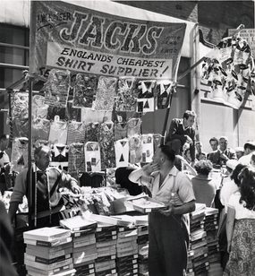 Black and white archive photograph of shoppers browsing a stall, advertised as 'Jacks: England's cheapest shirt supplier'